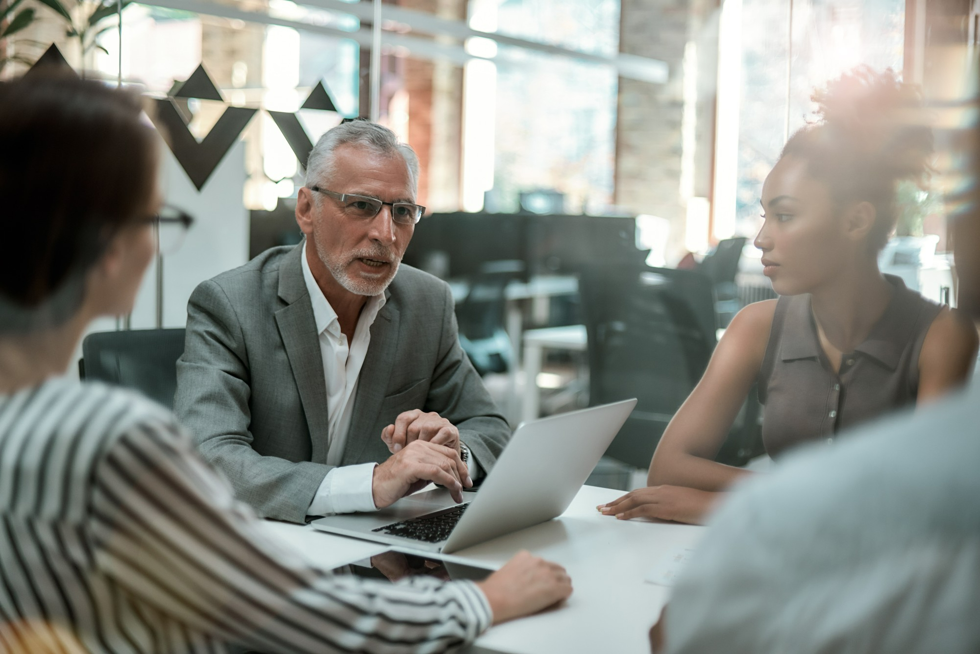 Colleagues in discussion around a laptop in a glass-walled office